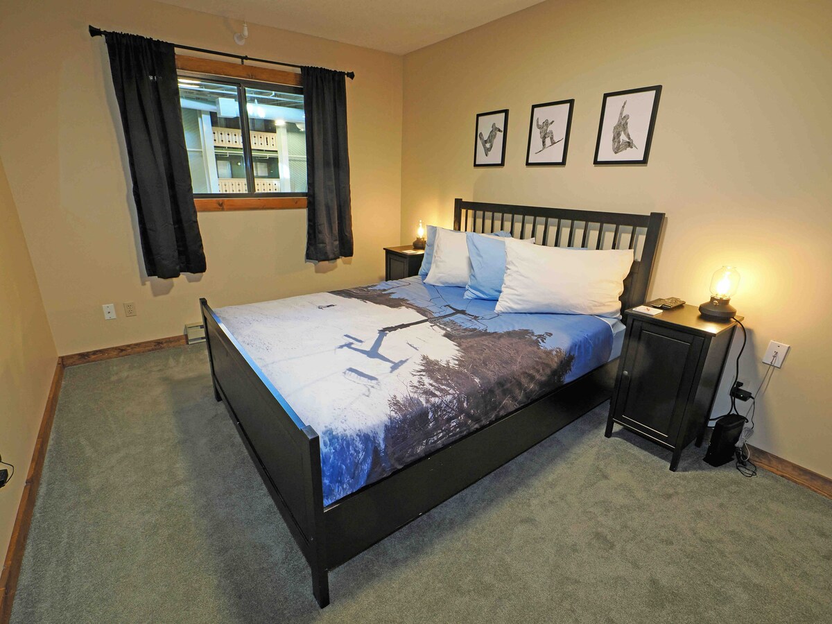 Gostinjska soba s bračnim krevetom i zidnim pametnim televizorom. 