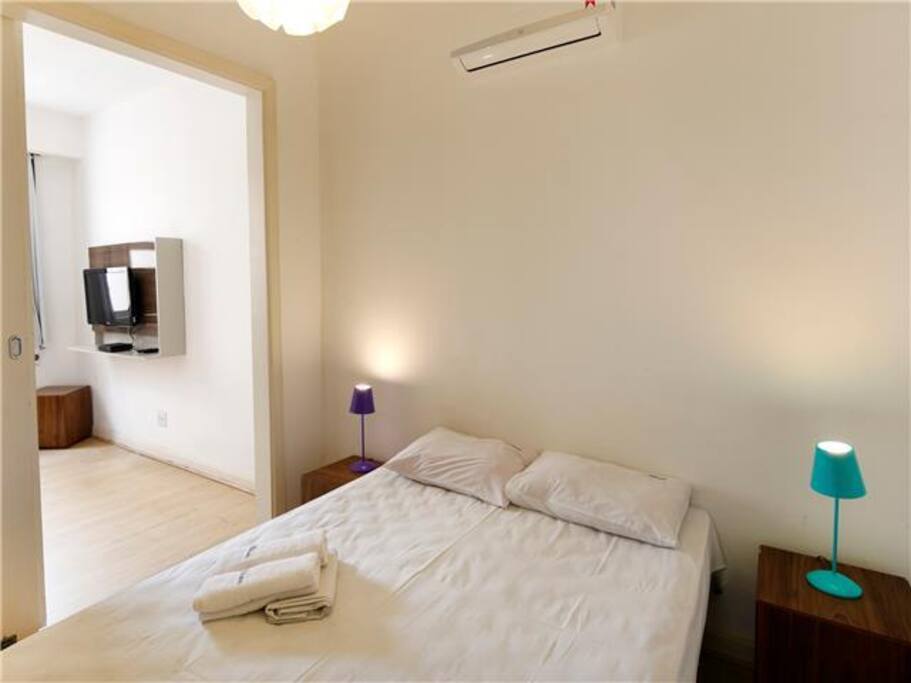 Ambiente com cama de casal e split e closet, e outro ambiente, com sofá-cama e ar condicionado de janela