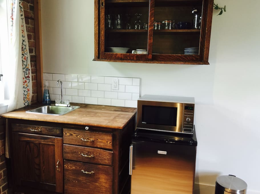 Kitchenette with antique cupboards, modern fixtures and appliances (microwave and fridge), dishes, etc. The little fridge even has a teeny freezer.