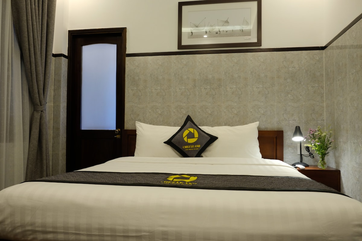 A comfortable sleeping area features a spacious bed dressed in crisp white linens and a decorative gray throw. A minimalistic lamp provides soft lighting beside the bed, while a fresh flower arrangement adds a touch of color. Textured wallpaper creates a cozy ambiance.