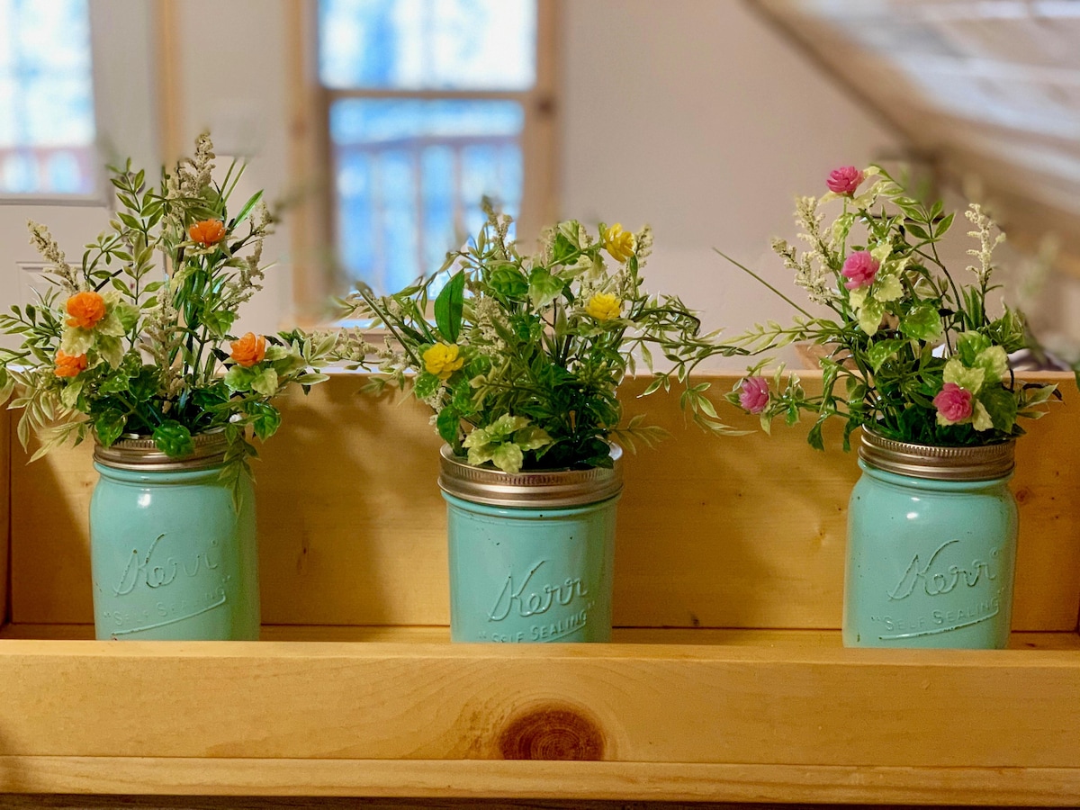 Three turquoise mason jars are placed on a wooden ledge, each filled with an assortment of artificial flowers in various colors. The jars provide a decorative touch, enhancing the serene interior ambiance.