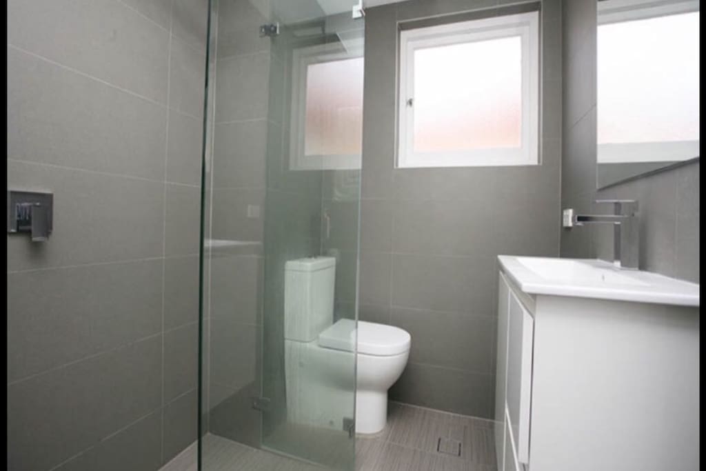 Modern and clean bathroom with large shower and stainless steel features with large mirror and heated towel rack.