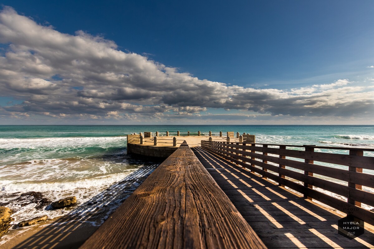 A wooden pier extends into the ocean, framed by gentle waves and soft sandy shores. The sky is filled with clouds reflecting the warm light, creating a serene backdrop for the tranquil waters. The structure invites leisurely strolls and offers scenic views of the coastline.