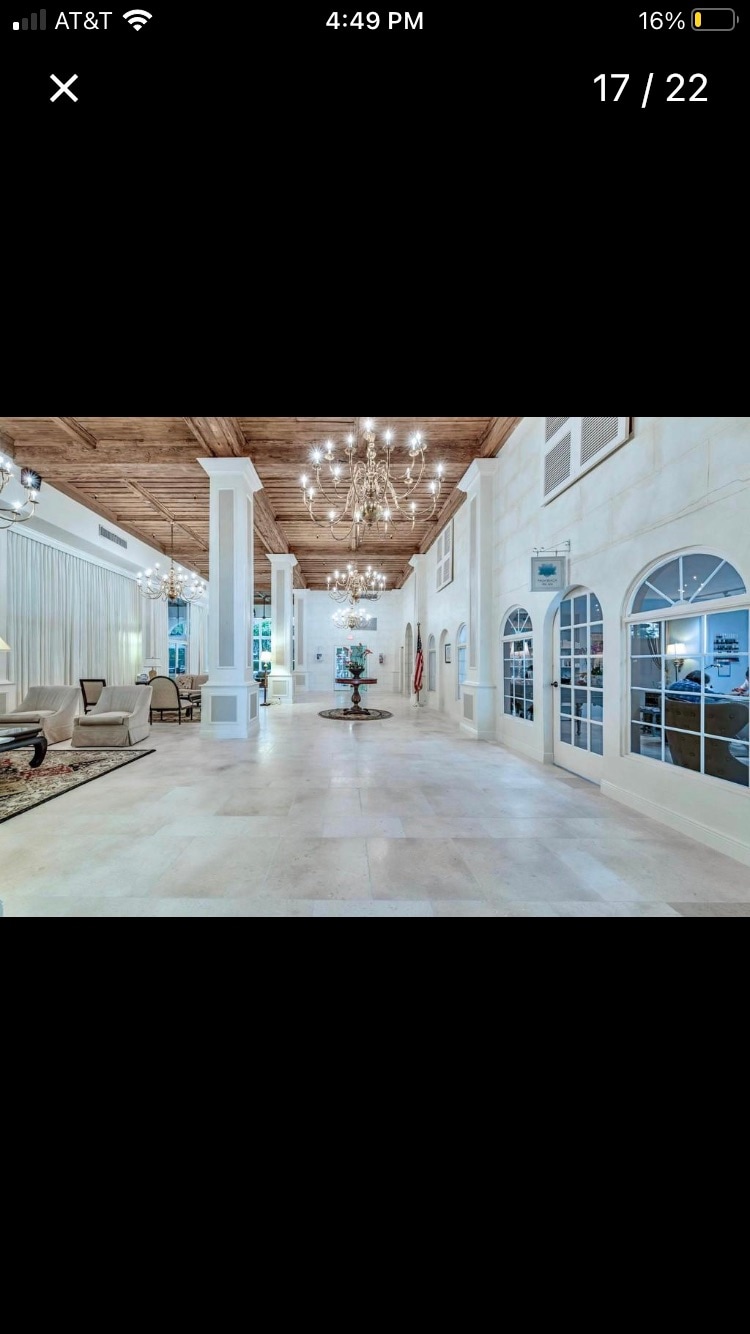 A bright and spacious lobby area features high ceilings adorned with elegant chandeliers. Marble flooring enhances the open space, which is accented by tall windows and archways. Comfortable seating areas are positioned throughout, providing a welcoming environment for guests.