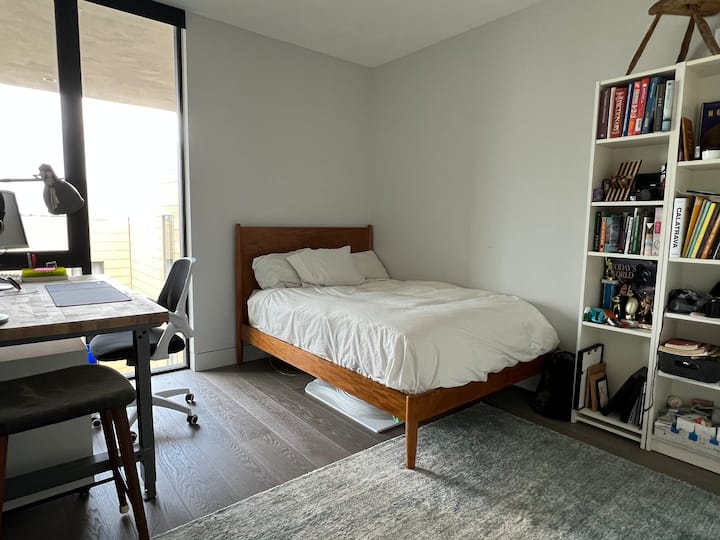 Dormitorio con cama de matrimonio y una gran ventana del suelo al techo con persianas enrollables. 