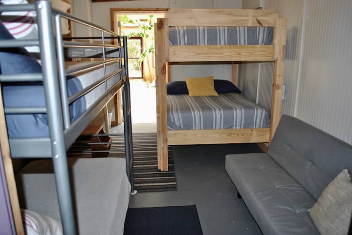 Спална соба 3/Куќа на спрат опремена со кревети на спрат во целосна големина, двокреветна соба и двоен кауч на спуштање. Надворешната врата води до градината и зелената куќа.