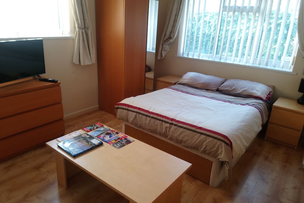A spacious double bed room with two chests of drawers, a sofa, coffee table, wardrobe with full length mirror and smart TV.