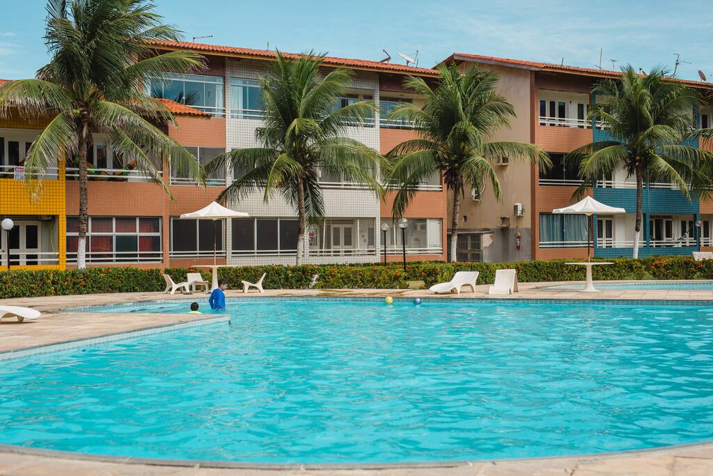Piscinas adulto e infantil em uma área de lazer rodeada por uma ampla área verde
