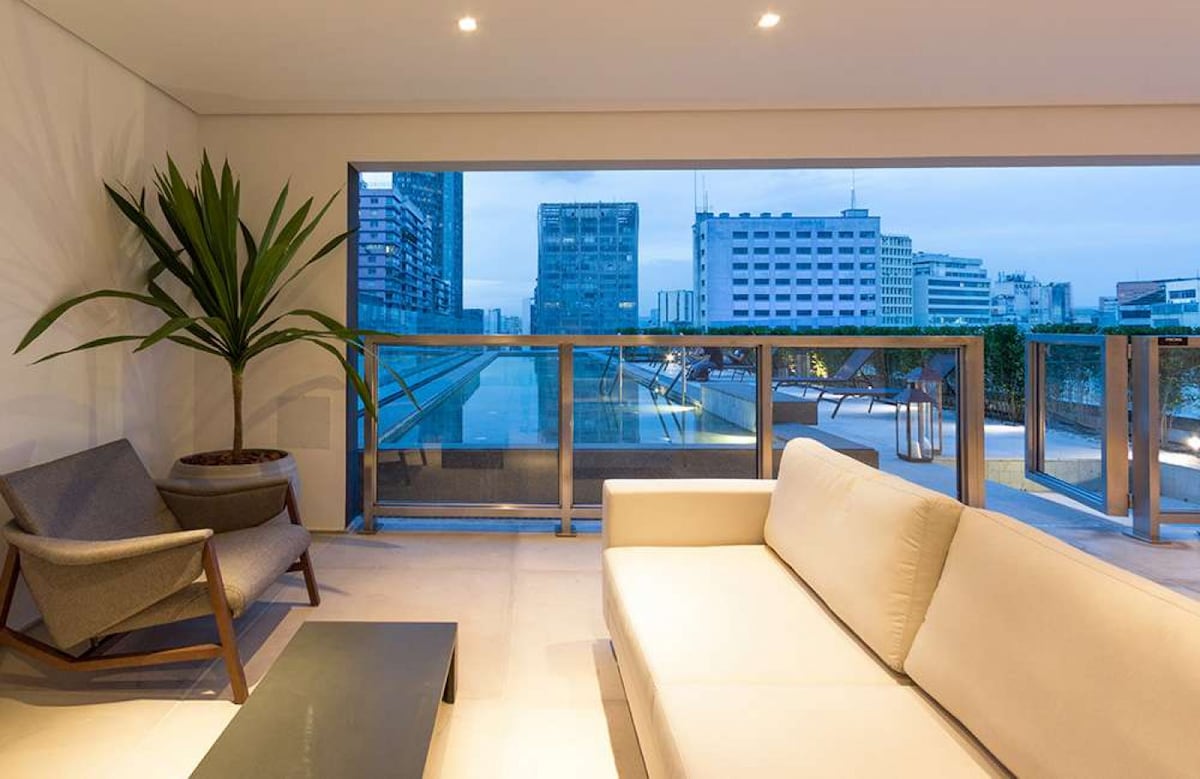 A modern seating area is visible, featuring a light-colored sofa and a dark coffee table. Large windows offer a view of the city skyline, framed by greenery. The space is illuminated with soft, natural light, creating a calm ambiance.