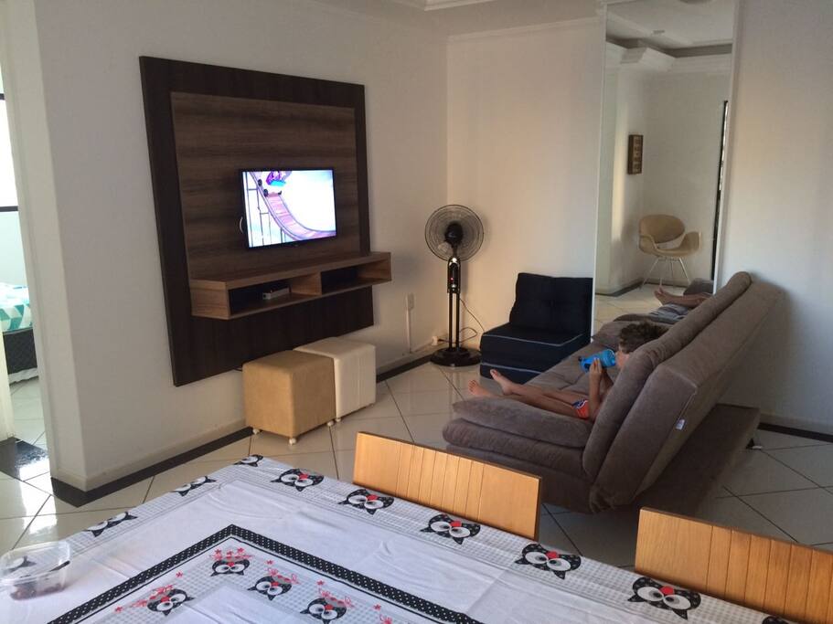 Sala de dois ambientes com mesa de jantar, sofá cama e TV a cabo.