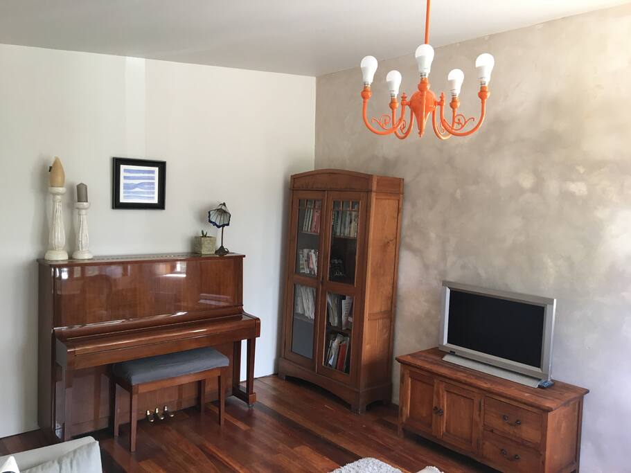 Living room with a TV, sofa bed, piano, basic kitchen facilities and desk.