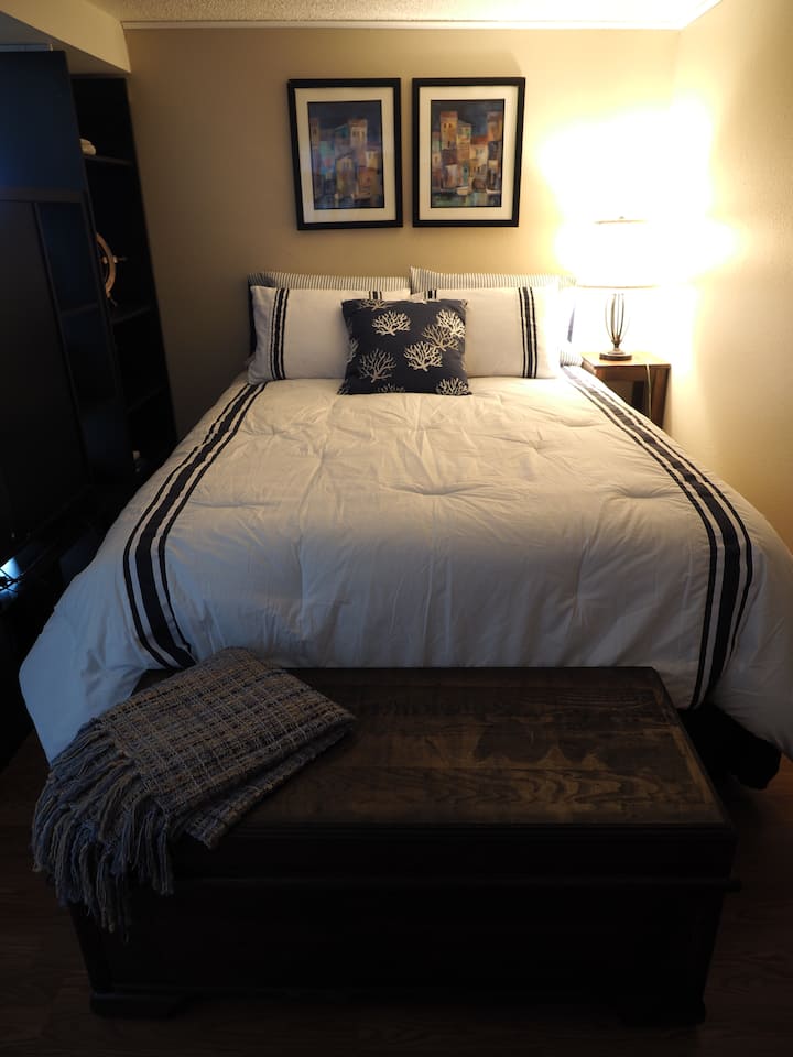 מיטת קווין סייז עם סדינים יוקרתיים מוסתרת מאחורי מפריד 8' ומספקת פרטיות לאזור השינה. 