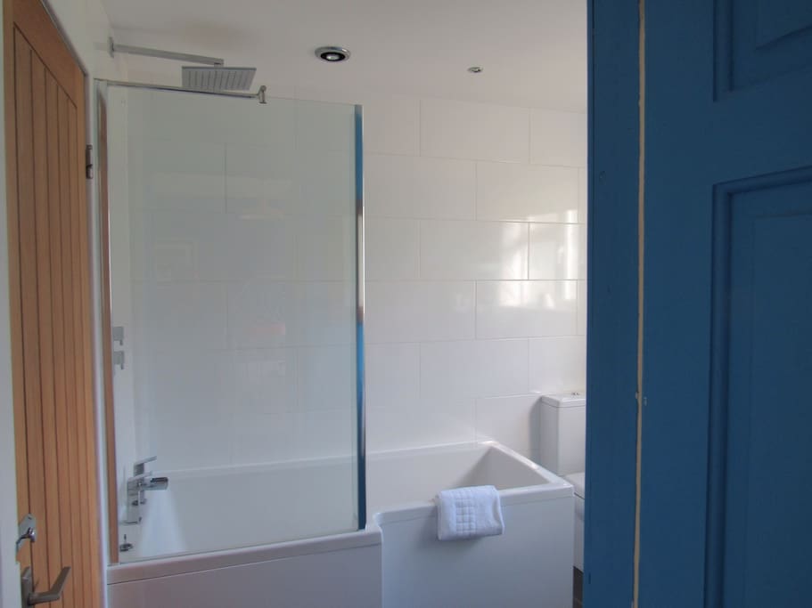 Modern ensuite bathroom with rain shower bath, sink, toilet, toiletries and towels provided
