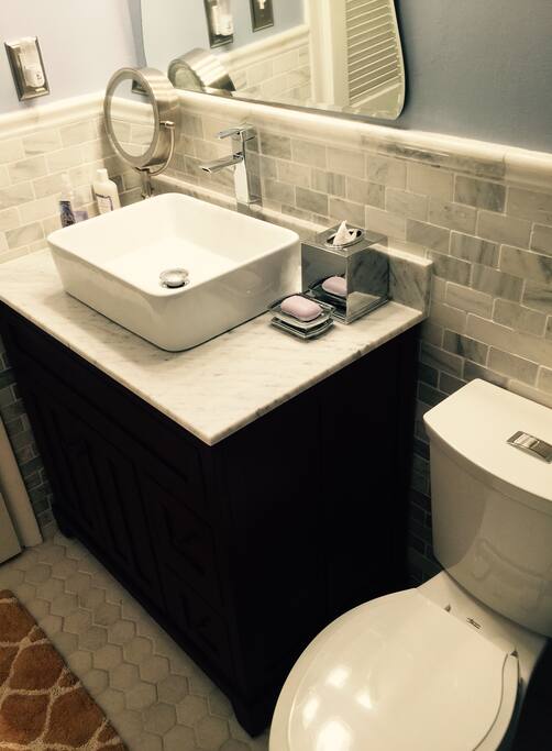 Beautiful new bathroom with marble tile on the floors and walls, new toilet, and new basin sink. The cabinet is made from cherry wood and topped with carrera marble.