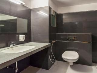 A modern bathroom showcases sleek, dark tiles on the walls and floor. A countertop with a built-in sink is positioned beneath a large mirror. A toilet is discreetly placed to one side, while a handheld shower fixture is available.