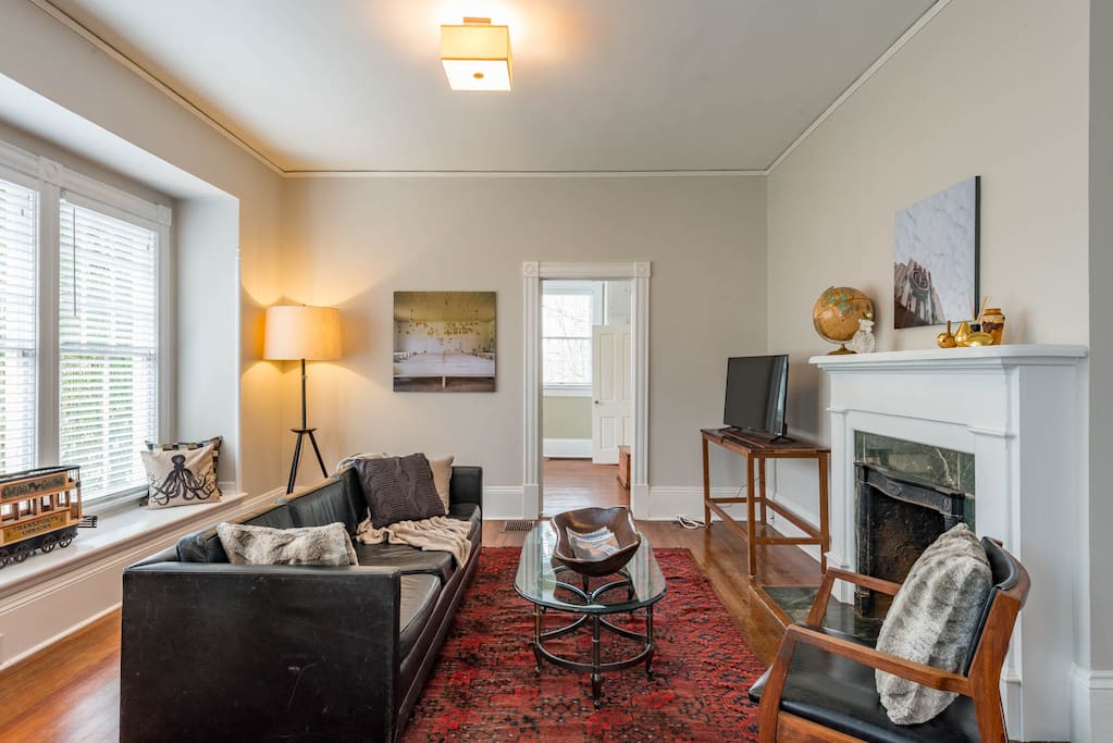 Living room from entry, leather couch, mid-century chair, antique oriental rug, fireplace, window seat, TV.