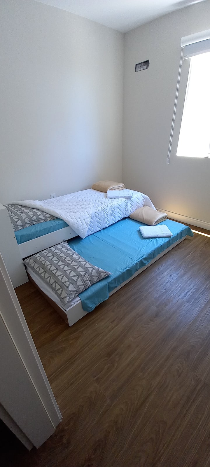 Ოთახი ორადგილიანი საწოლით, თარო კარით და რულონის ფარდით.