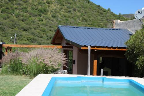 A detached house features a sloped metal roof and is complemented by lush greenery surrounding the outdoor pool. The scene conveys a serene setting with rolling hills in the background and a well-maintained lawn leading to the pool area.