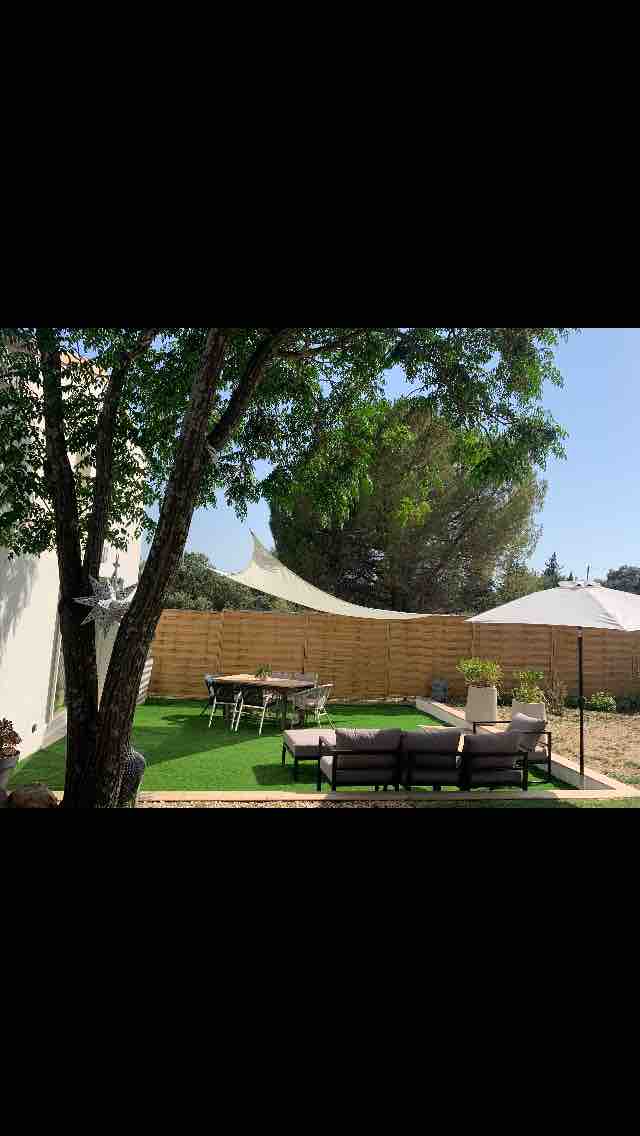 A well-maintained garden area is shown, featuring a comfortable seating arrangement under shade from a large umbrella. A dining table with chairs is present, accompanied by a sunshade. Lush greenery surrounds the space, enhancing the natural ambiance.