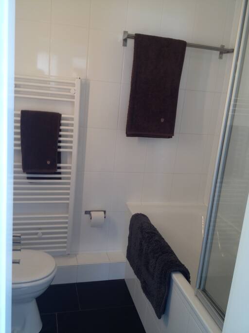 Neat white bathroom with a bath tub and a folding glass shower screen; heated towel rack.