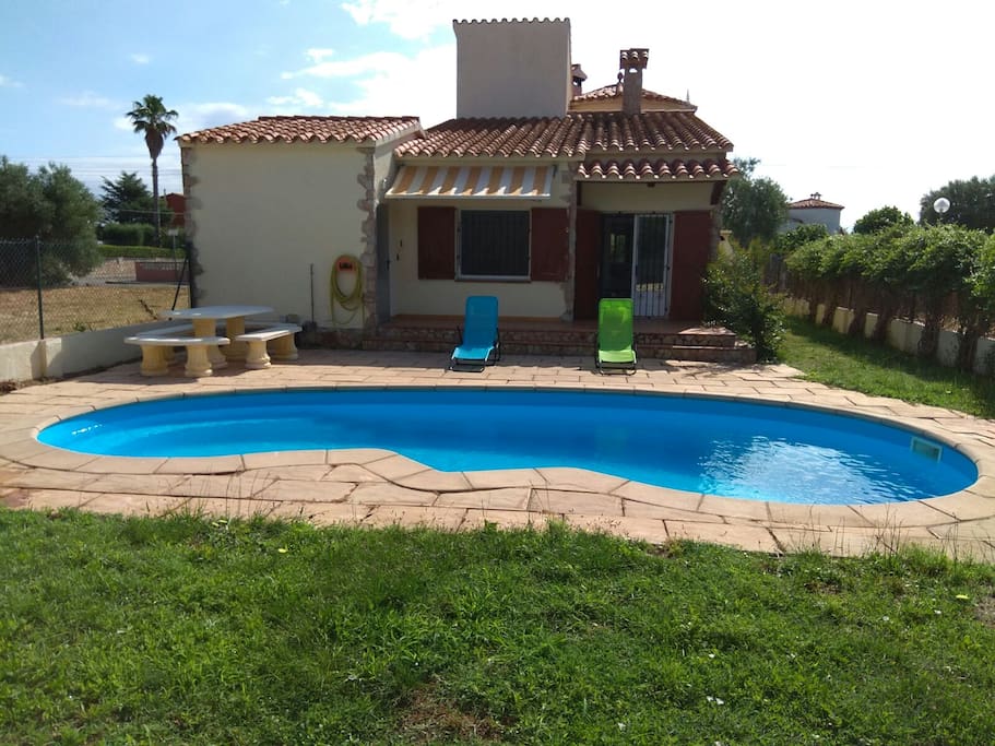 Patio trasero donde esta la piscina, la mesa de piedra, las tumbonas y una entrada al garaje donde esta la lavadora, plancha...