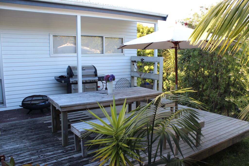 Outdoor entertaining area nestled in amongst a sub-tropical back drop. With BBQ, brazier, outdoor seating and umbrella.