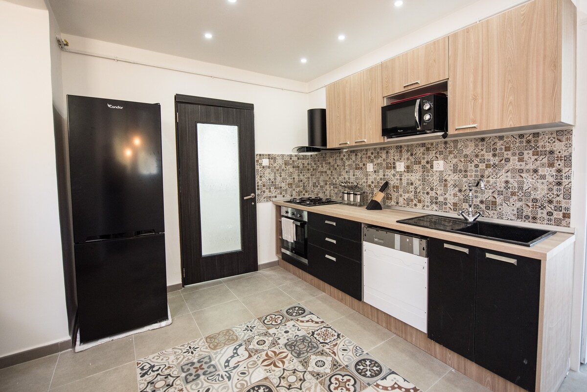 The kitchen features modern cabinetry with a combination of wood and dark finishes. A large refrigerator and a built-in microwave are included, alongside a stove and an ample workspace. A patterned tile floor adds character to the room, complemented by neutral wall tones.
