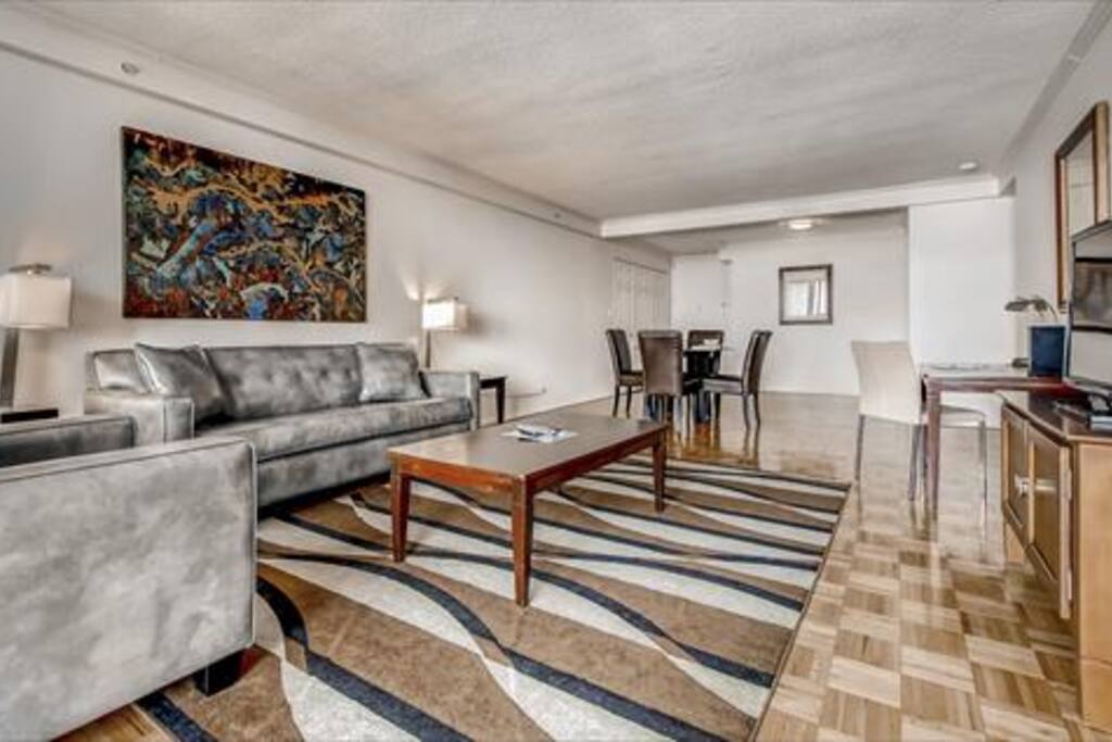 Spacious living room with sofa bed, club chair, entertainment center, convenient work desk and floor to ceiling windows