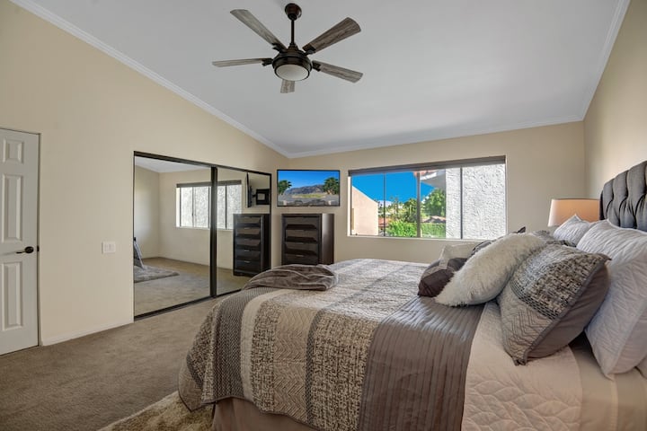 ห้องนอนใหญ่ขนาดใหญ่พร้อมตู้เสื้อผ้าแบบวอล์คอินและทิวทัศน์ของสระว่ายน้ำและทะเลทรายนอกหน้าต่างขนาดใหญ่