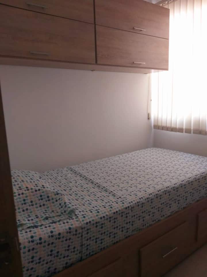 Tretia izba s jednolôžkom, dreveným stolom, horizontálnou skriňou a ventilátorom.