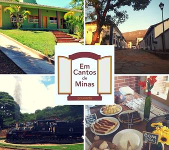 A serene setting is displayed, featuring a green building with a landscaped path. Nearby, quaint structures line a stone pathway. A vintage train can be seen in the background, while a dining table is set with traditional breakfast items, complemented by fresh flowers.