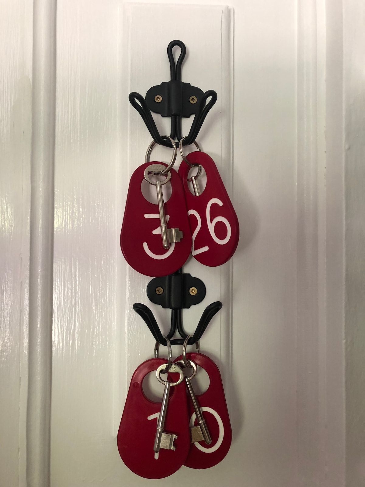 A wall-mounted key holder displays four red key tags, each numbered: 10, 26, and 32. The tags hang from black hooks, creating a simple and organized entryway feature.