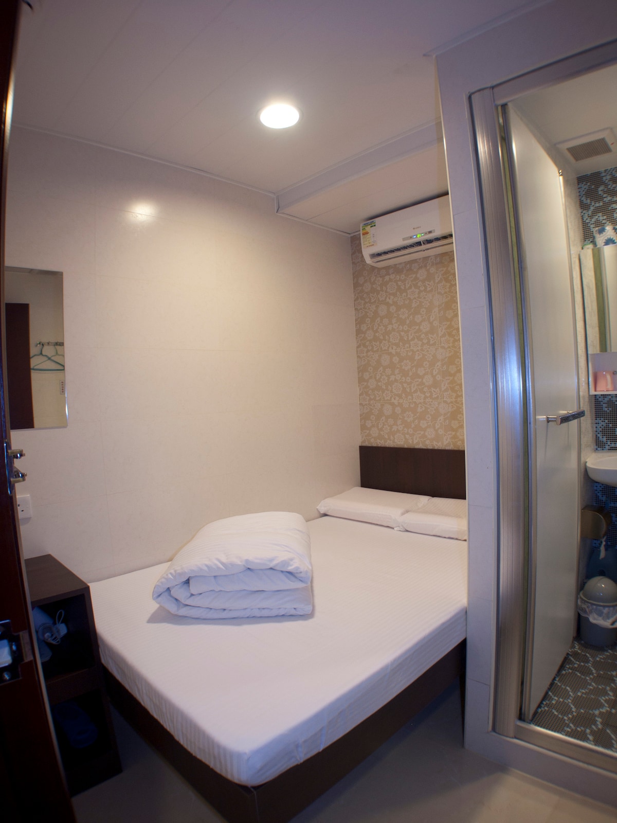 The room features a spacious bed with crisp white linens, complemented by neatly folded towels. A small closet is visible alongside a mirror, while a bathroom area is partitioned with glass, showcasing modern fixtures and tiles.