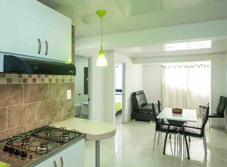 A modern kitchen features white cabinetry and a gas stove with a tiled backsplash. A round dining table with black chairs occupies the airy space, complemented by large windows that allow natural light to fill the room.