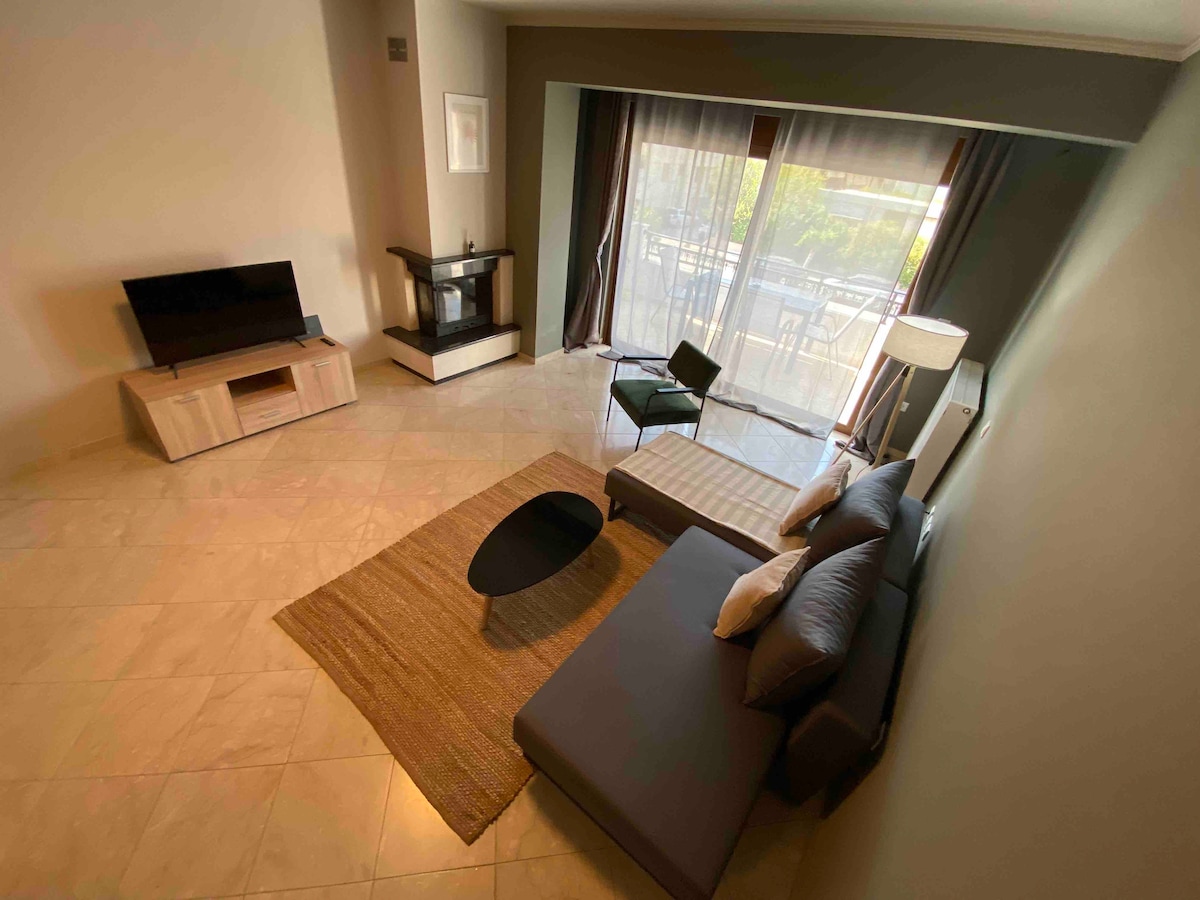 The spacious living area features a modern design with a comfortable sectional sofa, an energy-efficient fireplace, and a 44-inch television. A large window lets in natural light, while a rug and a pair of accent chairs add to the room's functionality.