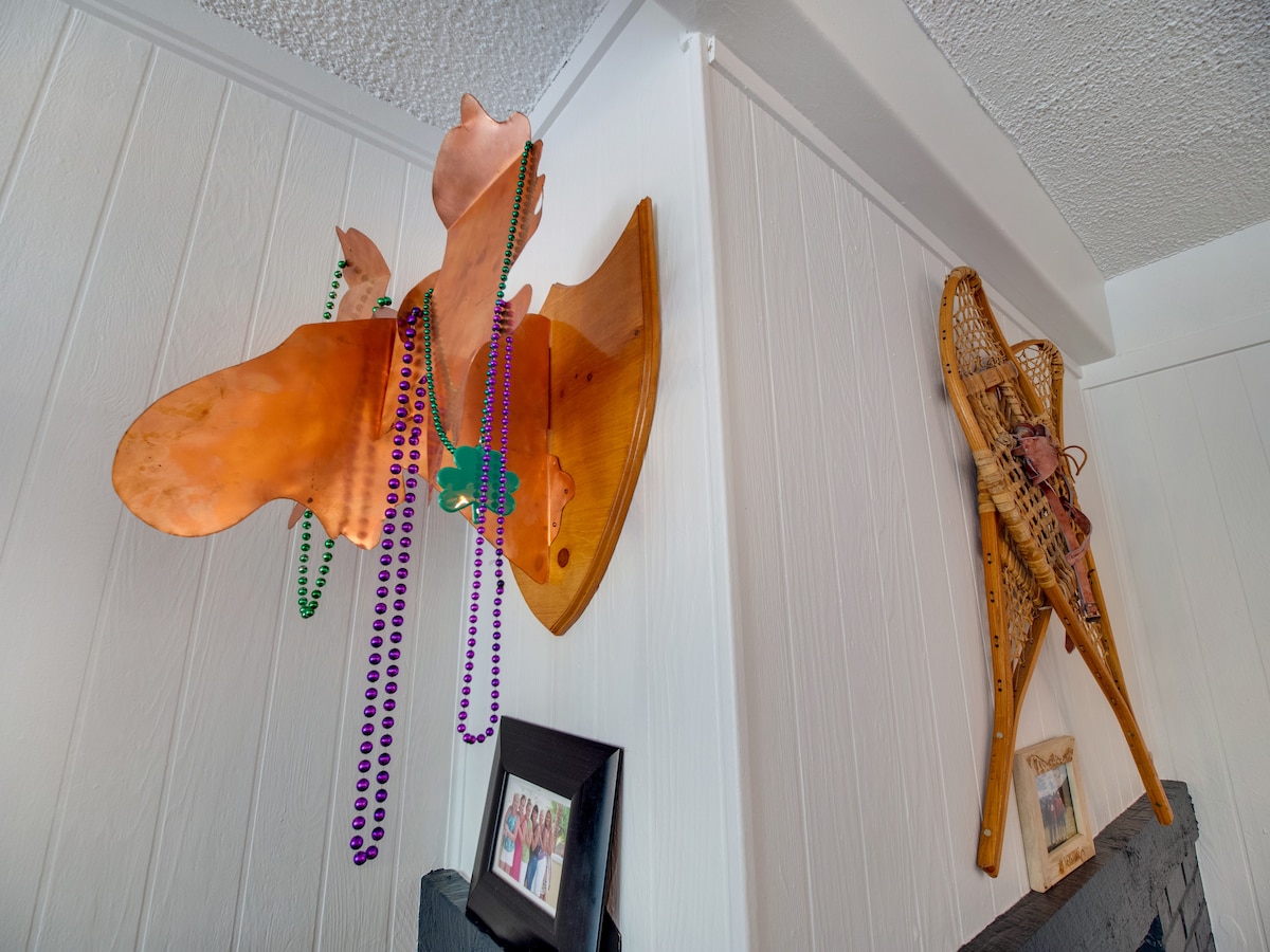 Decorative wall art includes a polished copper moose head and traditional snowshoes, adding a unique touch to the space. Colorful beaded necklaces hang from the moose, while framed photographs sit on a nearby shelf, enhancing the character of the room.