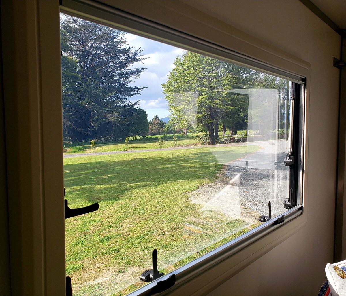 A wide-open window offers a view of the grassy landscape, framed by trees in the distance. Natural light floods the interior, highlighting the simplicity and connection to nature outside.