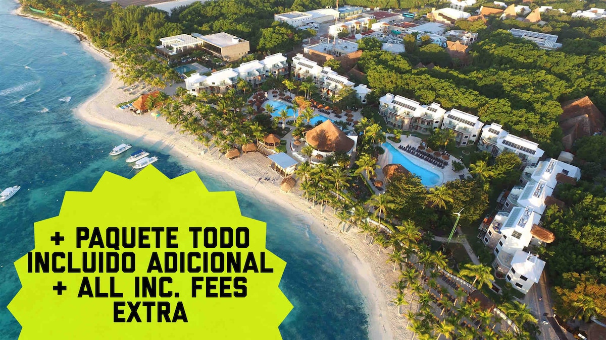 An aerial view of the resort reveals white-sand beaches bordered by lush tropical vegetation. The layout features multiple buildings along the shore, with swimming pools and amenities visible, harmonizing with the natural surroundings.