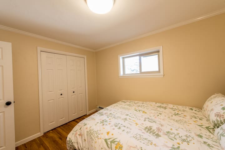 חדר שינה אמצעי עם מיטת קווין סייז, ארון מרווח ותריסים שחורים.