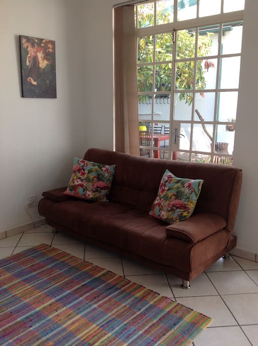 Open plan living area features full kitchen, small dining table, bookshelf and comfy sofa (turns into a bed) and armchair