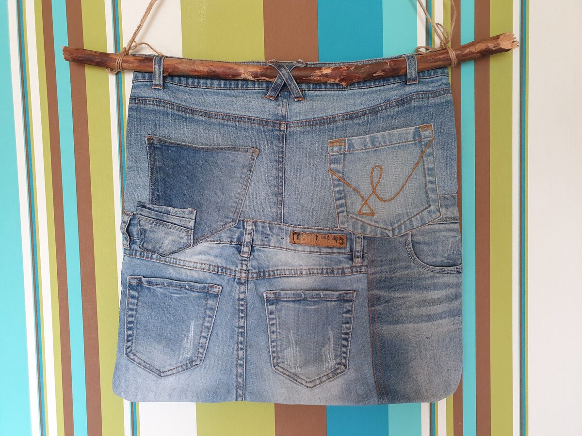 A decorative wall hanging displays a patchwork of denim pockets, creatively arranged to resemble a pair of jeans. The backdrop features vertical stripes in shades of teal, brown, and cream, adding a vibrant touch to the setting.