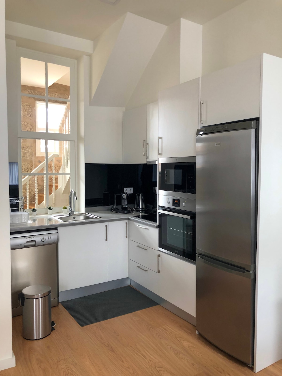 A modern kitchen is equipped with stainless steel appliances including a refrigerator, microwave, and dishwasher. A sleek countertop is complemented by a sink and coffee maker. Light enters through a nearby window, enhancing the bright and functional space.