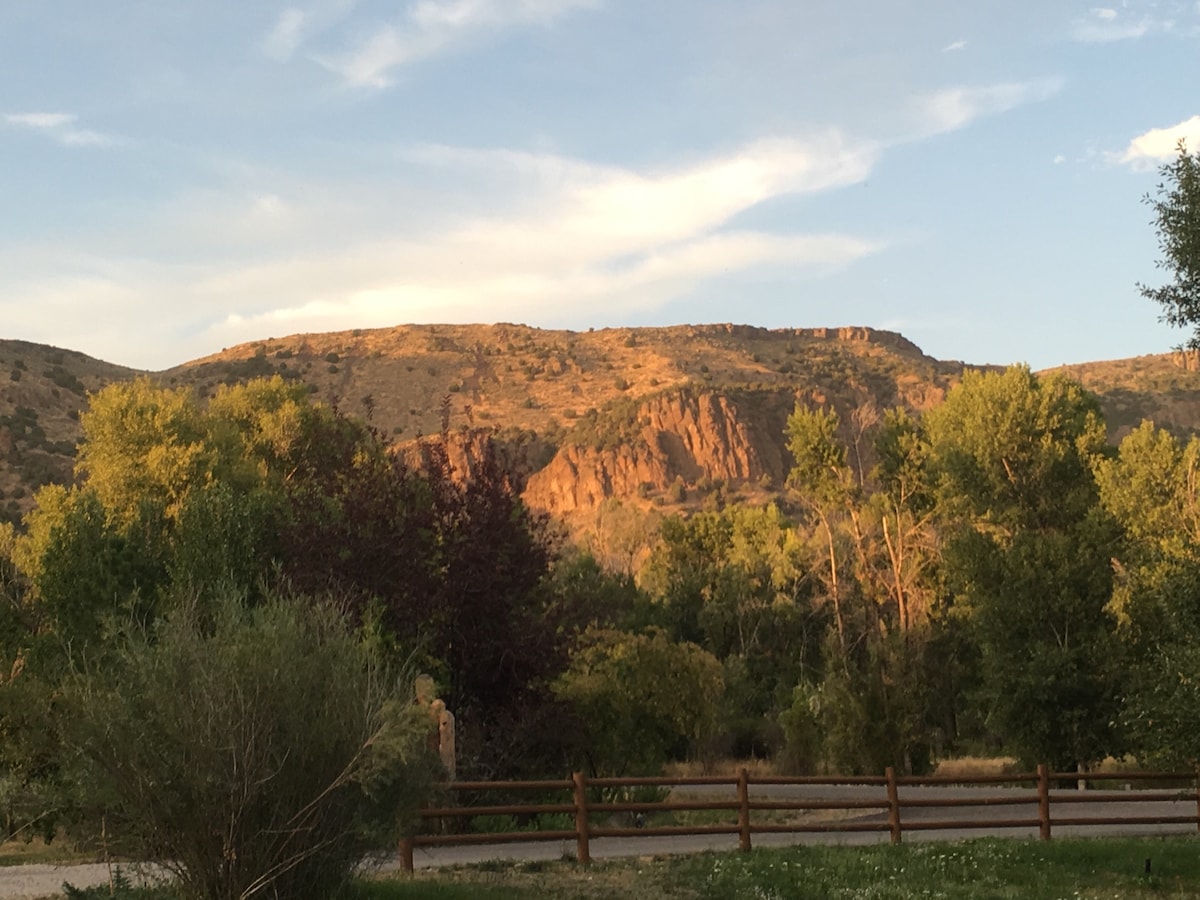 The image showcases a picturesque landscape featuring majestic hills bathed in warm golden light. Lush greenery surrounds the area, with various trees and shrubs in the foreground. A rustic wooden fence runs along the path, framing the scene against the backdrop of the tranquil hills.