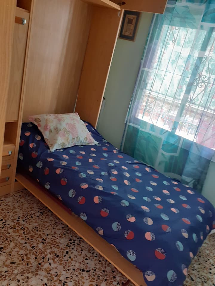 Cameră mică, simplă, cu pat pliant și birou și numeroase sertare și dulapuri. 