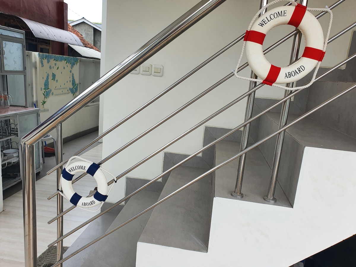 Two life rings are mounted on a modern metallic handrail next to a staircase. One ring features red and white stripes, while the other has blue and white stripes. A spacious area is visible in the background, contributing to the overall inviting atmosphere.