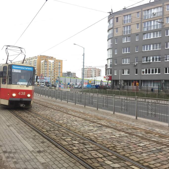 Вид на дом. В дали через дорогу виден супермаркет. Влево стадион 3 остановки. Вправо 1 остановка музей янтаря