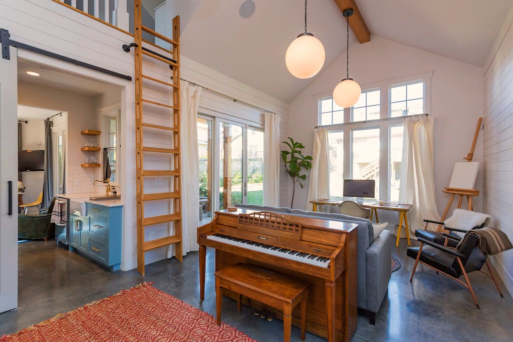 Main common area with Crate & Barrel sofa bed and ladder going up to loft. The ladder is operated by pulling the base away from the wall and then climbing up! The barn door separates this room from the rest of the house. (NOTE: sadly the piano was recently sold)