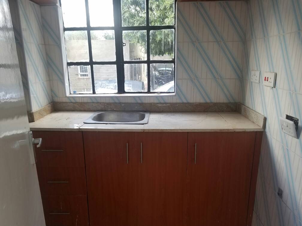 A compact kitchen space features wooden cabinetry with multiple storage compartments. A stainless steel sink is positioned against a window, allowing natural light to brighten the area. Blue and white patterned tiles adorn the walls, providing a clean and airy backdrop.