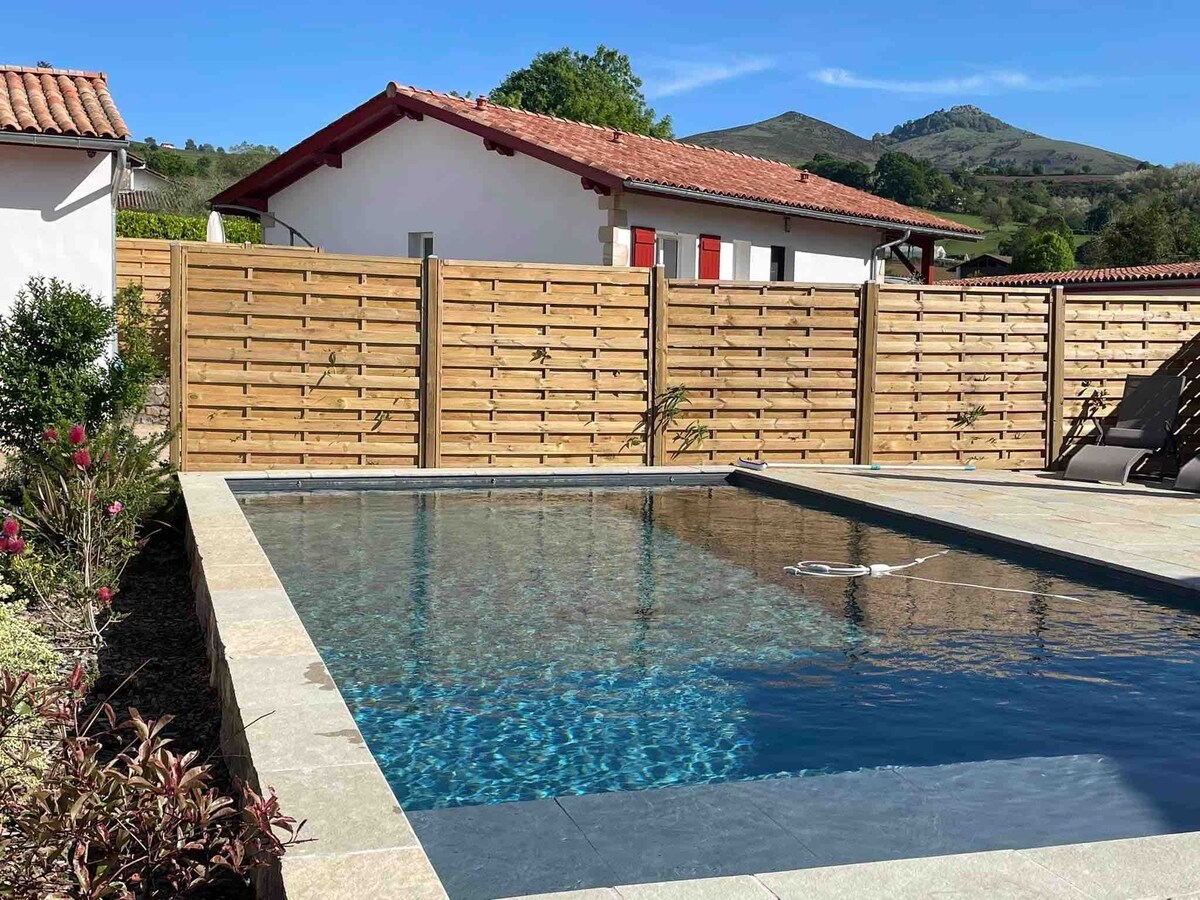 A private heated saltwater pool is surrounded by a stone patio and wooden privacy fencing. The pool's clear water reflects the sunlight, and lounge chairs are positioned nearby, providing a tranquil space for relaxation. The farmhouse and mountain scenery are visible in the background.