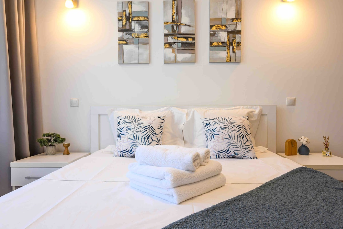 A serene sleeping area is presented with a spacious bed adorned with plush pillows. Decorative wall art adds a touch of elegance above the bed. Soft lighting is provided by two sconces, enhancing the calm and cozy atmosphere of the room.